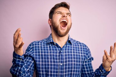 Sakallı, mavi gözlü, deli deli dikilmiş, sinirli bir ifadeyle bağıran, kollarını kaldırmış genç, yakışıklı sarışın bir adam. Hayal kırıklığı konsepti.