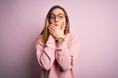 Mavi gözlü, pembe arka planda süveter ve gözlük takan güzel sarışın kadın yanlışlıkla elleri ile ağzını kapatırken şok oldu. Gizli konsept.