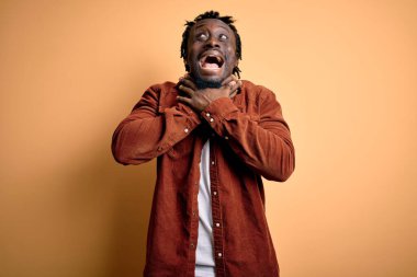 Sarı arka planda dikilen ve boğularak can çekişen sıradan bir ceket giyen yakışıklı Afro-Amerikan erkeği. Sağlık problemi. Boğulma ve intihar konsepti.