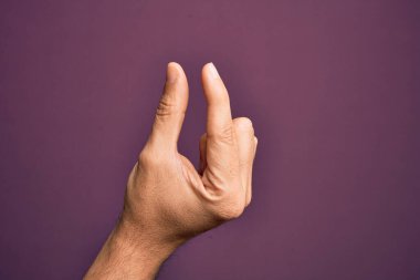 İzole edilmiş mor arka plan üzerinde parmaklarını gösteren beyaz bir adamın eli. Görünmez bir şeyi alıyor, parmakları boşluğu gösteren bir nesneyi tutuyor.