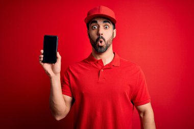 Sakallı, akıllı telefonlu yakışıklı teslimatçı sürpriz bir yüzle korkmuş ve korku ifadesinden heyecanlanmış yemek uygulaması sunuyor.