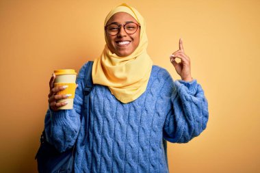 Müslüman tesettürlü ve gözlüklü Afro Amerikalı genç bir kadın bir fikir ya da soru işareti ile şaşırmış bir şekilde kahve içiyor.