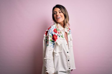 Moda kıyafetleri giyen genç ve güzel bir kadın. Manken, sokak tarzı giyiniyor. Pembe arka planda dikiliyor.