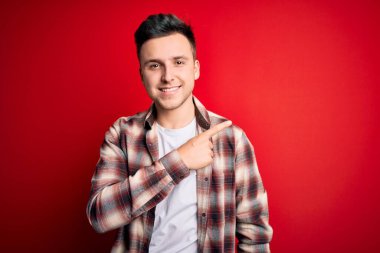 Kırmızı izole edilmiş arka plan üzerine gündelik modern tişört giyen yakışıklı beyaz bir adam. Yüzünde mutlu ve doğal bir ifadeyle el ve parmak uçlarını gösteren bir gülümseme var.