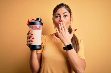 Genç, güzel esmer kadın, diyet içeceği ile birlikte spor şişesi tutuyor. Ağzını kapatıyor. Ağzı hata payı utançla dolu.