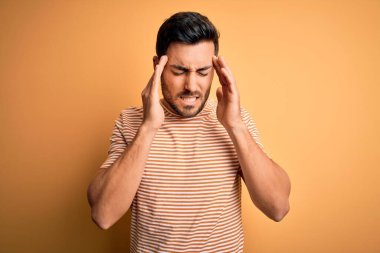 Sakallı, sarı arka planda sıradan çizgili tişörtler giyen, başı ağrıyan genç, yakışıklı bir adam. Migren ağrısı..