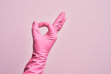 İzole edilmiş pembe arka plan üzerinde temizlik eldiveni olan beyaz bir gencin eli. Onaylanmış yüz ifadesi, parmaklarıyla iyi bir sembol oluşturuyor.