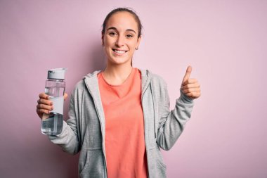 Genç, güzel, sportif bir kadın, ferahlatıcı su şişesi içiyor, gülümsüyor ve gülümsüyor.