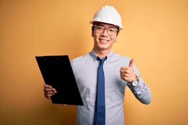 Güvenlik kaskı takan yakışıklı Çinli mühendis elinde kocaman bir gülümsemeyle mutlu. Tamam işareti yap, parmaklarınla başparmağını kaldır, mükemmel işaret.