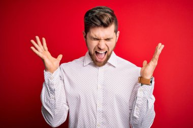 Sarışın, sakallı ve mavi gözlü genç bir işadamı kırmızı arka planda zarif bir gömlek giyerek başarıyı kutluyor. Kolları havada ve gözleri kapalı heyecanla bağırıyor. Kazanan konsept