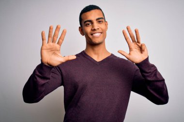 Beyaz arka plan üzerine gündelik süveter giyen genç ve yakışıklı Afro-Amerikan adam dokuz numaralı parmaklarıyla işaret ederken kendinden emin ve mutlu bir şekilde gülümsüyor..