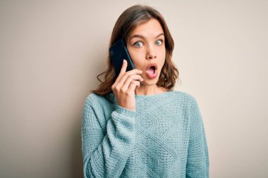 Sarışın genç bir kız, gizli bir arka planda akıllı telefondan konuşuyor. Şaşırmış bir yüzle korkmuş ve korku ifadesinden heyecanlanmış.