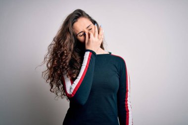 Kıvırcık saçlı genç bir kadın izole edilmiş beyaz arka planda günlük süveter giyiyor. Burnunu ve gözlerini ovuşturup yorgunluk ve baş ağrısı çekiyor. Stres ve hüsran kavramı.