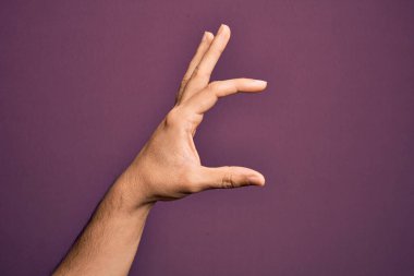 İzole edilmiş mor arka plan üzerinde parmaklarını gösteren beyaz bir adamın eli. Görünmez bir şeyi alıyor, parmakları boşluğu gösteren bir nesneyi tutuyor.