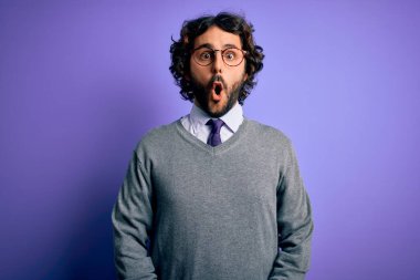 Sakallı, kravatlı, gözlüklü, mor arka planda duran yakışıklı bir iş adamı. Şaşırtıcı bir ifade, korku ve heyecanlı bir yüz ifadesi..