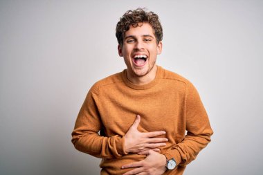 Sarışın, kıvırcık saçlı, beyaz arka planda sıradan bir süveter giyen, gülen ve kahkahalarla gülen genç bir adam..