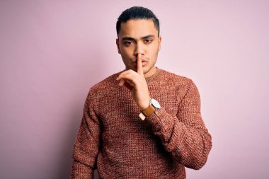 İzole edilmiş pembe arka planda günlük süveter giyen genç Brezilyalı adam sessiz olmak istiyor. Sessizlik ve gizli konsept.