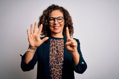 Orta yaşlı esmer iş kadını gözlüklü, izole edilmiş beyaz arka plan üzerinde duruyor ve altı numaralı parmaklarıyla işaret ederken kendinden emin ve mutlu bir şekilde gülümsüyor..