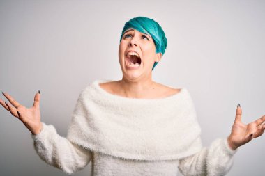 Mavi saçlı genç bir kadın beyaz arka plan üzerine sıradan bir süveter giyiyor deli deli deli bağırıyor ve bağırıyor agresif bir ifade ve kollar havada. Hayal kırıklığı konsepti.