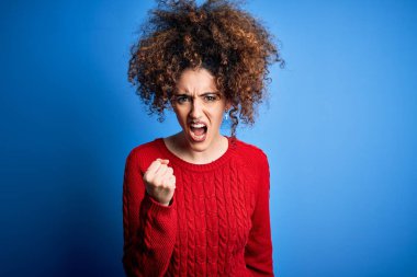 Kıvırcık saçlı ve piercingli genç bir kadın öfkeyle bağırırken kızgın ve kızgın bir şekilde yumruk kaldırıyor. Öfke ve agresif kavram.