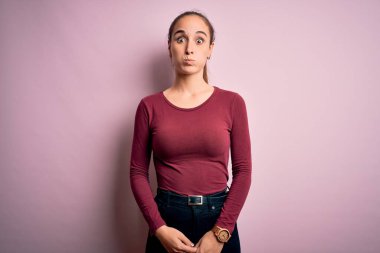 Gündelik tişört giyen genç ve güzel bir kadın izole edilmiş pembe arka planda durup komik yüzlü yanakları şişiriyor. Havayla şişmiş ağız, çılgın bir ifade..