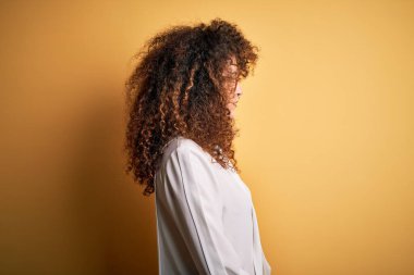 Kıvırcık saçlı, piercing takan ve yan tarafa bakan genç ve güzel esmer kadın, rahat profil pozu, kendine güvenen gülümsemesi olan doğal bir poz..