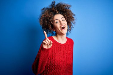 Kıvırcık saçlı ve piercingli, sıradan kırmızı kazak giyen genç ve güzel bir kadın başarılı bir fikri işaret ediyor. Heyecanlı ve mutlu. Bir numara..