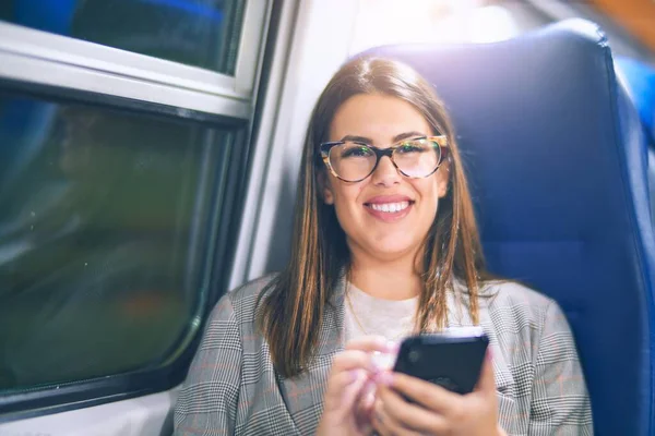 若い美しい女性が幸せと自信を笑顔 電車で移動するスマートフォンを顔に笑顔でお座り — ストック写真