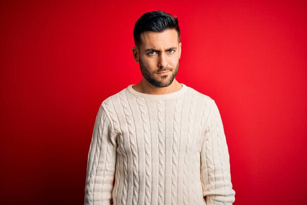 Young handsome man wearing casual white sweater standing over isolated red background skeptic and nervous, frowning upset because of problem. Negative person.