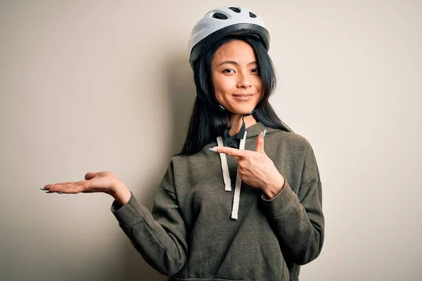 若いです美しいです中国の女性身に着けています自転車ヘルメット上の隔離された白い背景に驚いて 手で提示しながら 指で指してカメラに笑顔 — ストック写真