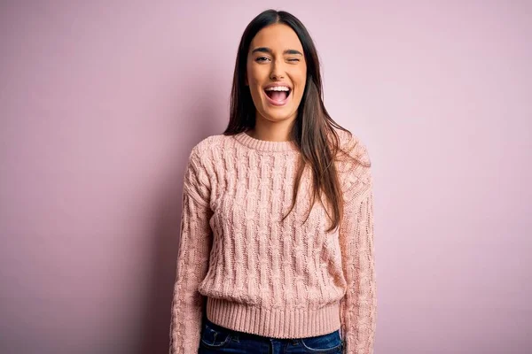 Young beautiful brunette woman wearing casual sweater over isolated pink background winking looking at the camera with sexy expression, cheerful and happy face.