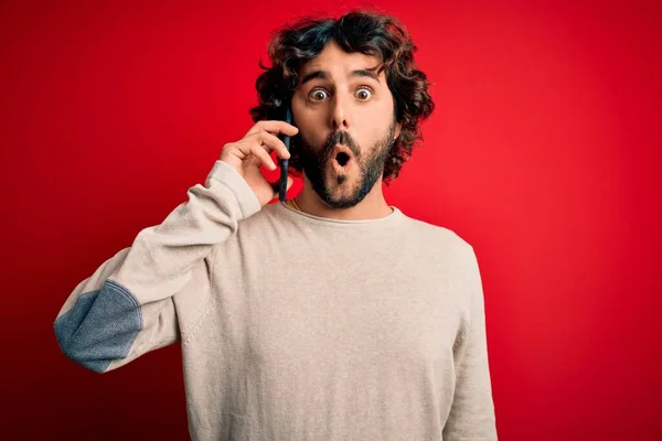 Pohledný Muž Vousy Při Rozhovoru Smartphonu Přes Červené Pozadí Vyděšený — Stock fotografie