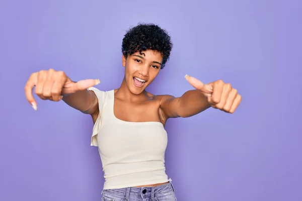 年轻美丽的非洲裔美国女人 身穿紫色背景的休闲T恤 手握积极的手势 微笑着竖起大拇指 为成功感到高兴 赢的手势 — 图库照片