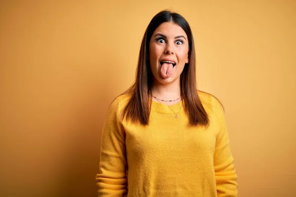 黄色の隔離された背景にカジュアルなセーターを着た若い美しい女性が面白い表情で幸せ舌を突き出しています 感情概念 — ストック写真