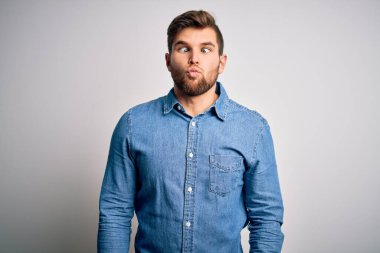 Sakallı, mavi gözlü, sıradan kot gömlekli, dudaklı, garip ve komik yüzlü genç yakışıklı sarışın adam. Komik ifade.