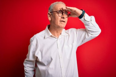Orta yaşlı yakışıklı, beyaz gömlekli, kırmızı arka planda gözlüklü, mutlu ve gülümseyen bir adam. Konsept aranıyor.