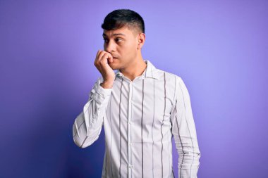 Mor arka planda duran zarif iş gömleği giyen genç, yakışıklı İspanyol adam elleri ağız yiyen tırnaklarla gergin ve stresli görünüyor. Endişe sorunu.