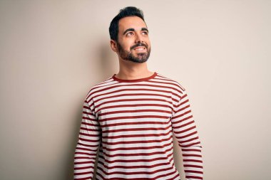 Sakallı, sıradan çizgili tişörtlü, beyaz arka planda duran, yüzünde gülümseme, doğal bir ifade olan genç yakışıklı bir adam. Kendinden emin gülen.