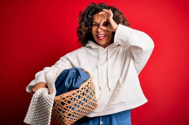 Orta yaşlı, sepet tutan güzel bir kadın yalnız kırmızı arka planda giysileri olan mutlu bir yüzü olan ve el ele verip parmaklarından içeri bakan bir kadın.