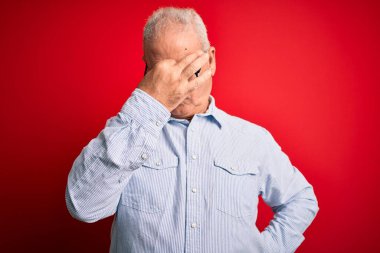 Orta yaşlı, beyaz, sıradan çizgili gömlek giyen, kırmızı arka planda gözlük takan, burnu ve gözleri ovuşturan, yorgun ve başı ağrıyan yakışıklı bir adam. Stres ve hüsran kavramı.