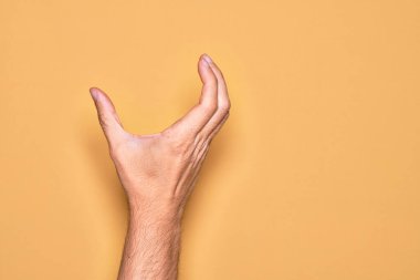 İzole edilmiş sarı arka plan üzerinde parmaklarını gösteren beyaz bir adamın eli. Görünmez bir şeyi alıp, parmaklarıyla uzayı gösteren bir nesneyi tutuyor.