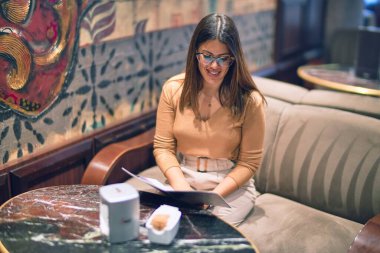 Mutlu ve kendinden emin gülümseyen genç ve güzel bir kadın. Barda yüzünde gülümsemeyle kanepede oturmak.