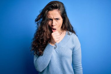 Kıvırcık saçlı, mavi süveter giyen, kendini iyi hissetmeyen ve soğuk algınlığı veya bronşitin belirtisi olarak öksüren genç ve güzel bir kadın. Sağlık hizmeti kavramı.