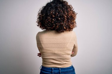 Genç ve güzel kıvırcık Arap kadın, beyaz arka plan üzerinde günlük tişört ve gözlük takıyor.