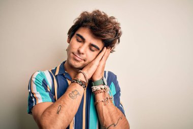 Yaz tatilindeki genç adam, renkli bir gömlek giyer, izole beyaz arka planda durur, uyur, yorgun düşler kurar, ellerle poz verir, kapalı gözlerle gülümserdi..