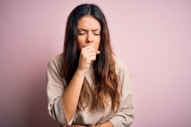 Genç ve güzel esmer bir kadın pembe arka planda dikilmiş, soğuk algınlığı ya da bronşitin belirtisi olarak öksürüyor. Sağlık hizmeti kavramı.