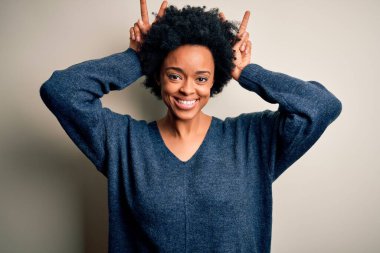 Genç, kıvırcık saçlı, kıvırcık saçlı, komik ve çılgın pozlar veren, parmakları tavşan kulaklı, neşeli gülümseyen güzel Afro-Amerikan kadın.