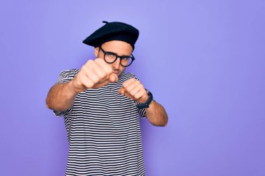 Mor arka planda mavi gözlü yakışıklı adam çizgili tişört ve Fransız beresi giyiyor. Yumruk yumruğa, agresif ve öfkeli saldırı, tehdit ve şiddet.