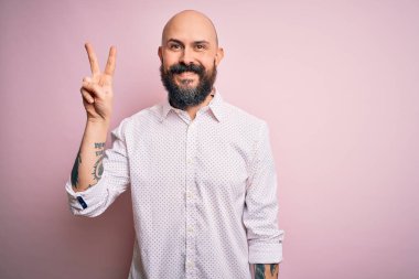 Sakallı yakışıklı, zarif gömlekli, soyutlanmış pembe arka planda iki numaralı parmaklarını gösterip gülümseyen, kendinden emin ve mutlu bir adam..