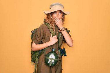 Mavi gözlü, sırt çantalı ve su mataralı genç sarışın kaşif kadın yanlışlıkla ağızlarını kapatmış. Gizli konsept.